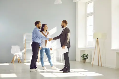Young married couple make deal, buy new house and exchange handshake with relator.